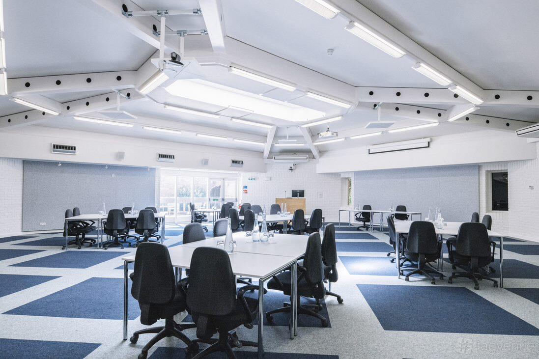 A meeting room with skylights, geometric ceiling design, and clustered tables with black chairs at Ashridge House.