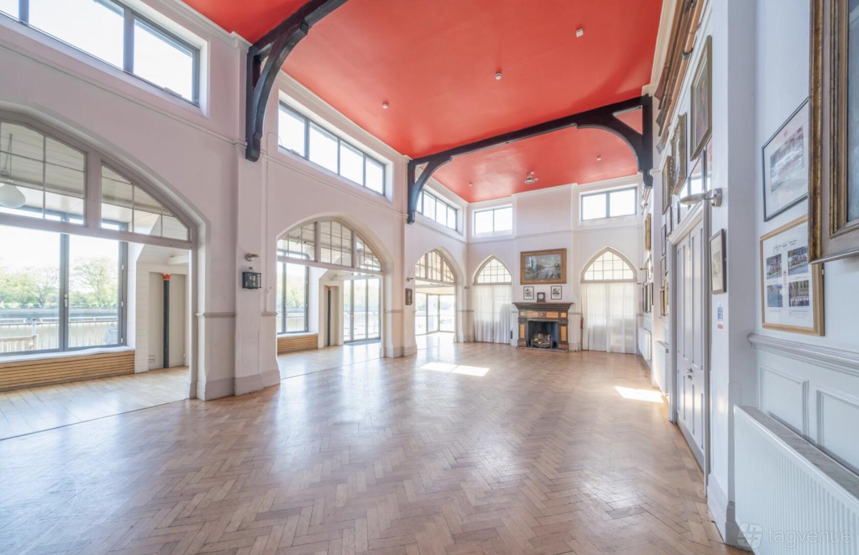 An event venue with high arched windows, herringbone wood floors, and a red ceiling at Thames Rowing Club.