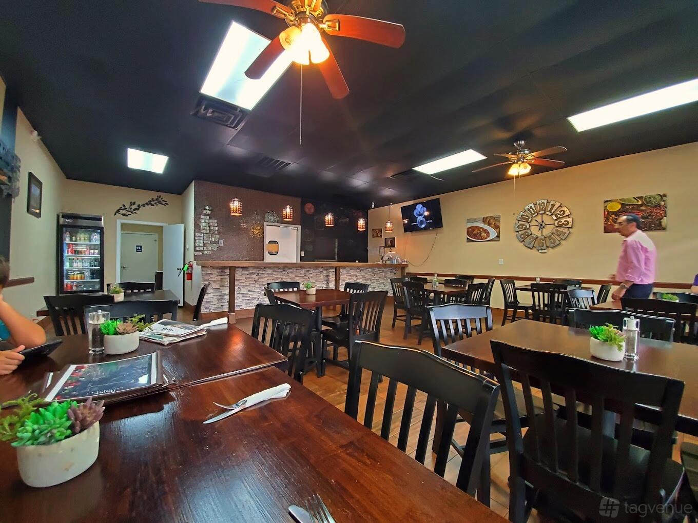 A restaurant dining area with dark wooden chairs, potted succulents on tables, and ceiling fans at Dino's Mediterranean Cuisine.