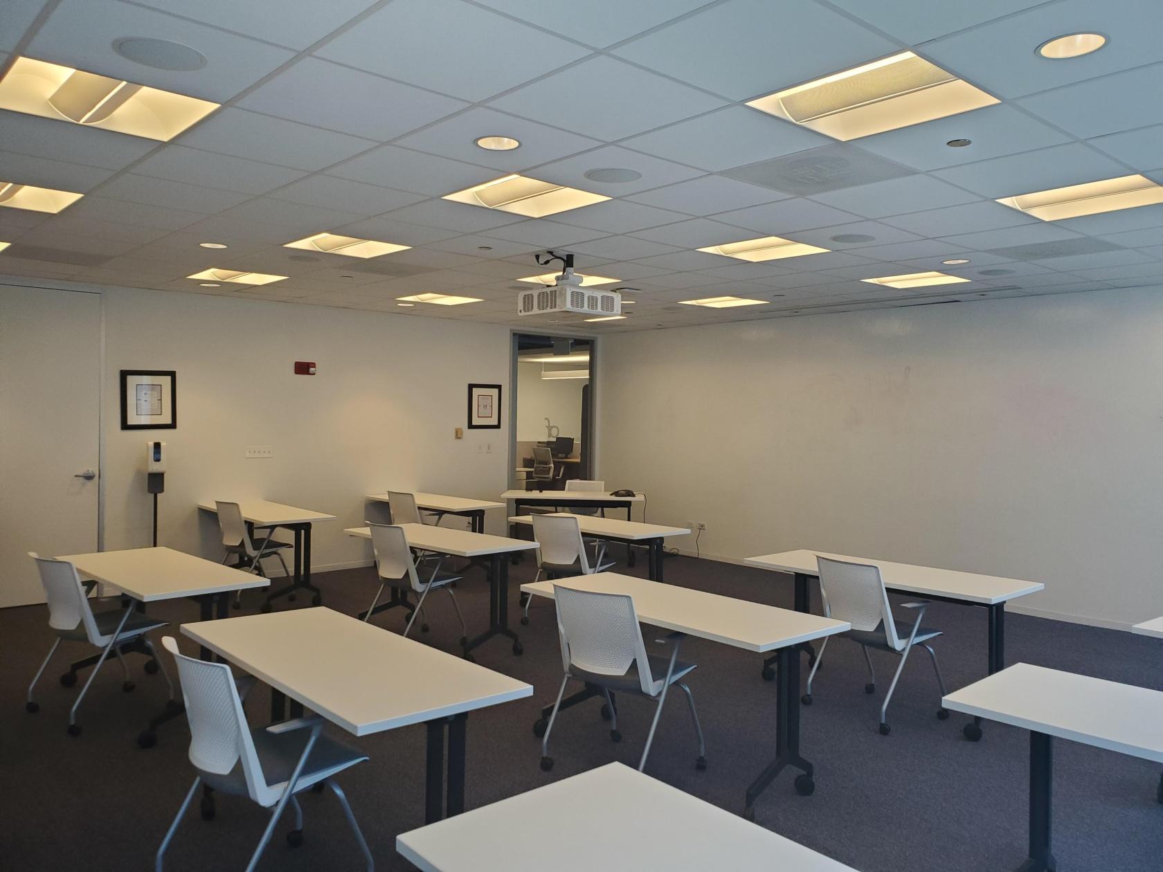 A community centre with rows of white tables, ergonomic chairs, and a ceiling projector at Association Forum.
