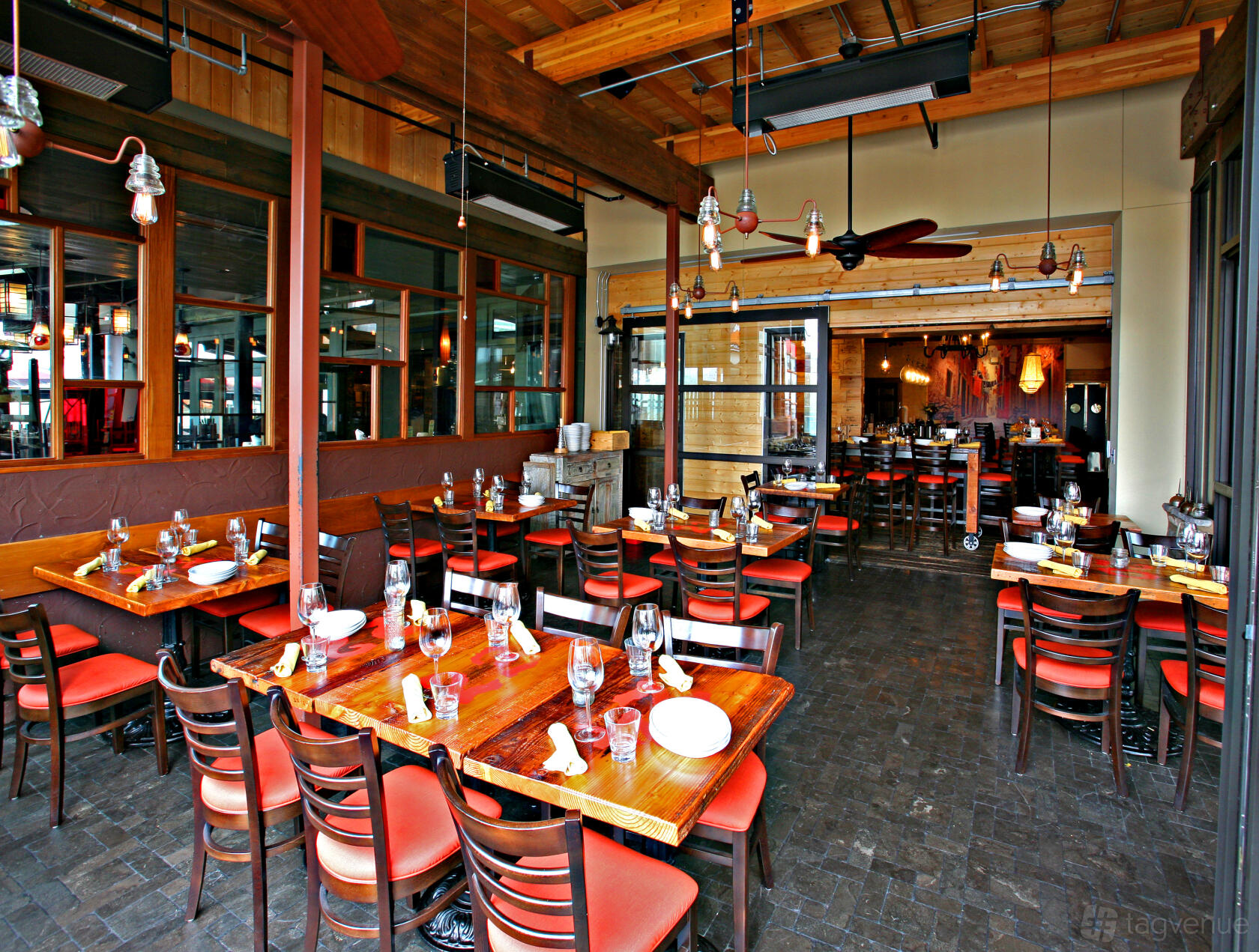 A restaurant with wooden tables, red cushioned chairs, and large windows at Davanti Enoteca - Del Mar.