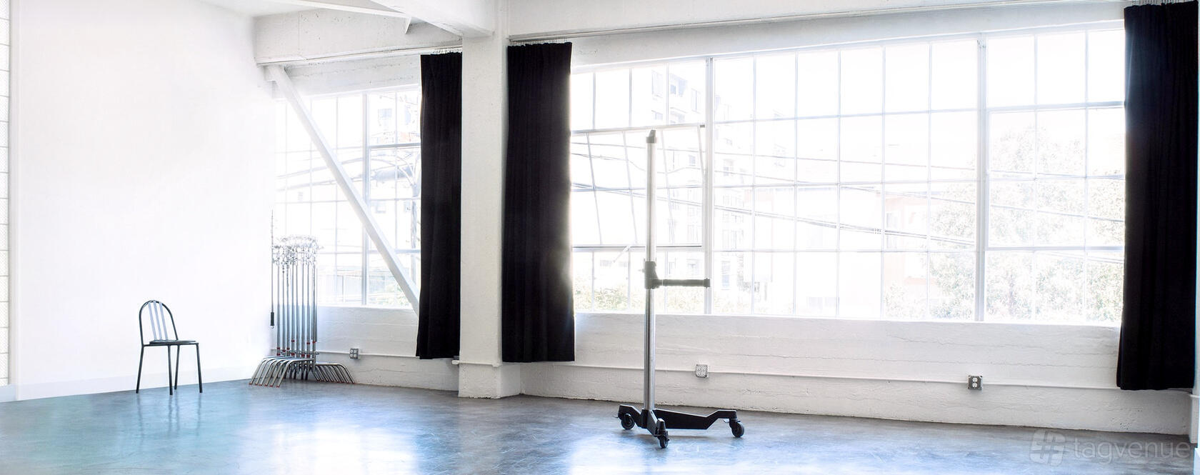 A photo studio with floor-to-ceiling windows, blackout curtains, concrete floors, and a rolling garment rack at Strobespace.
