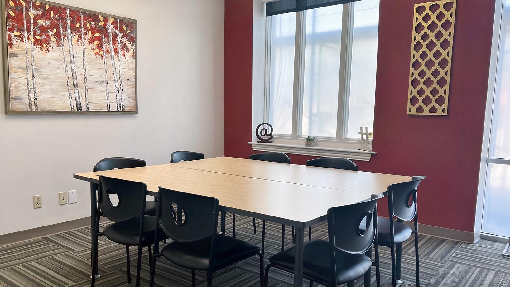 A meeting room with a rectangular table, eight black chairs, and large window at Ensemble Coworking.