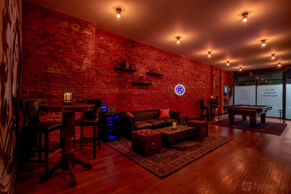 An event venue lounge with exposed brick walls, leather sofas, a pool table, and warm ceiling lighting at Social Cues - Vogue.