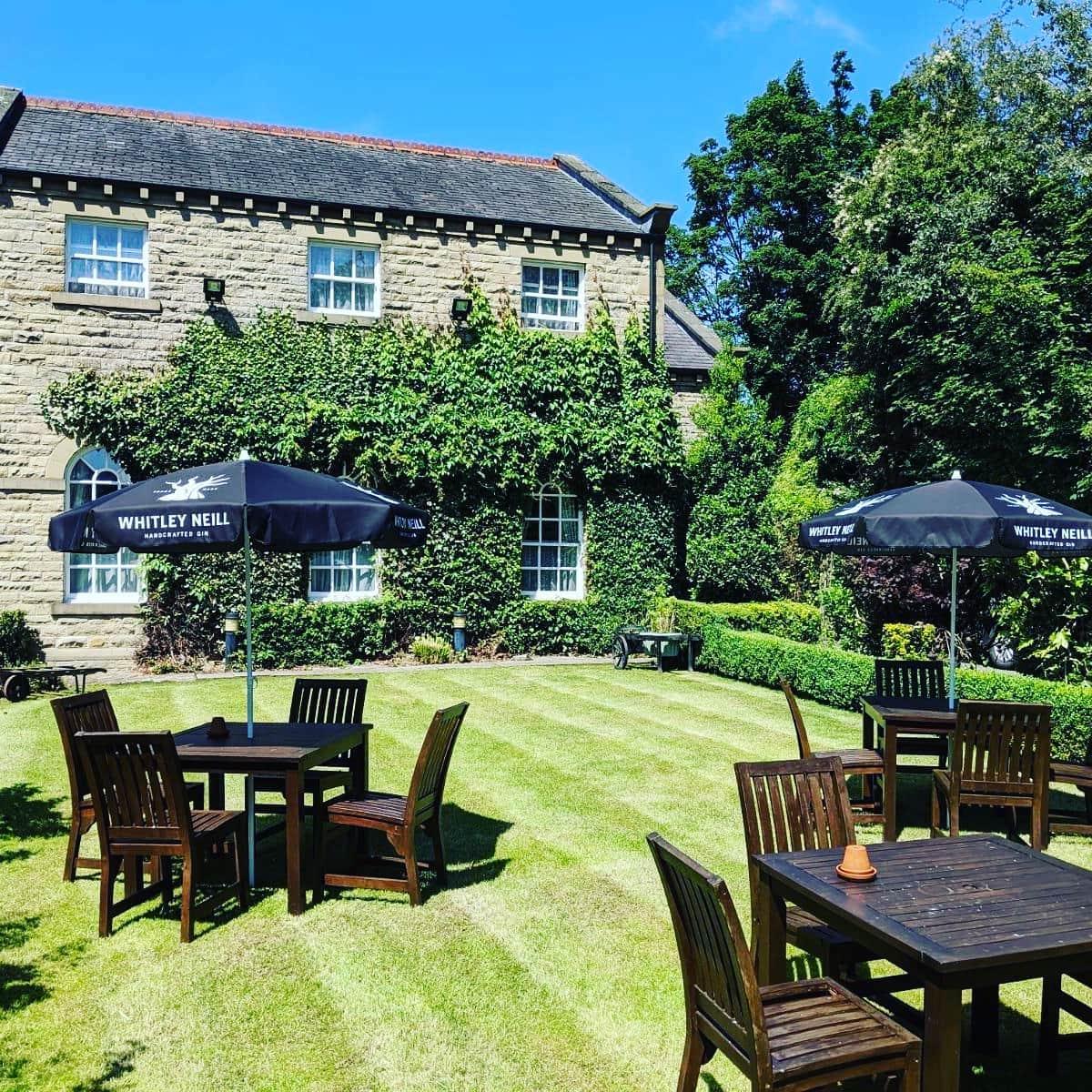 A hotel garden with wooden outdoor tables, lawn umbrellas, and ivy-covered stone walls at Healds Hall.