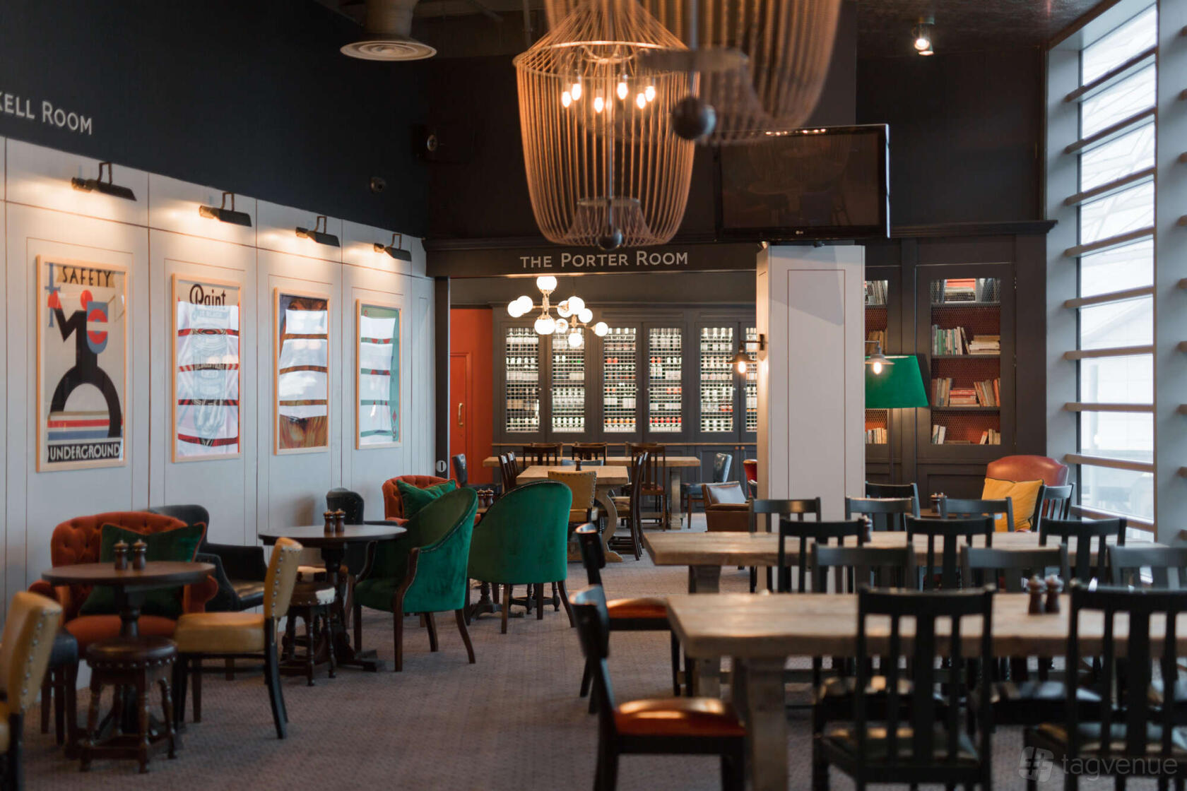 A dining room with eclectic chairs, round and rectangular tables, vintage posters, and bookshelf walls at The Bull Westfield.