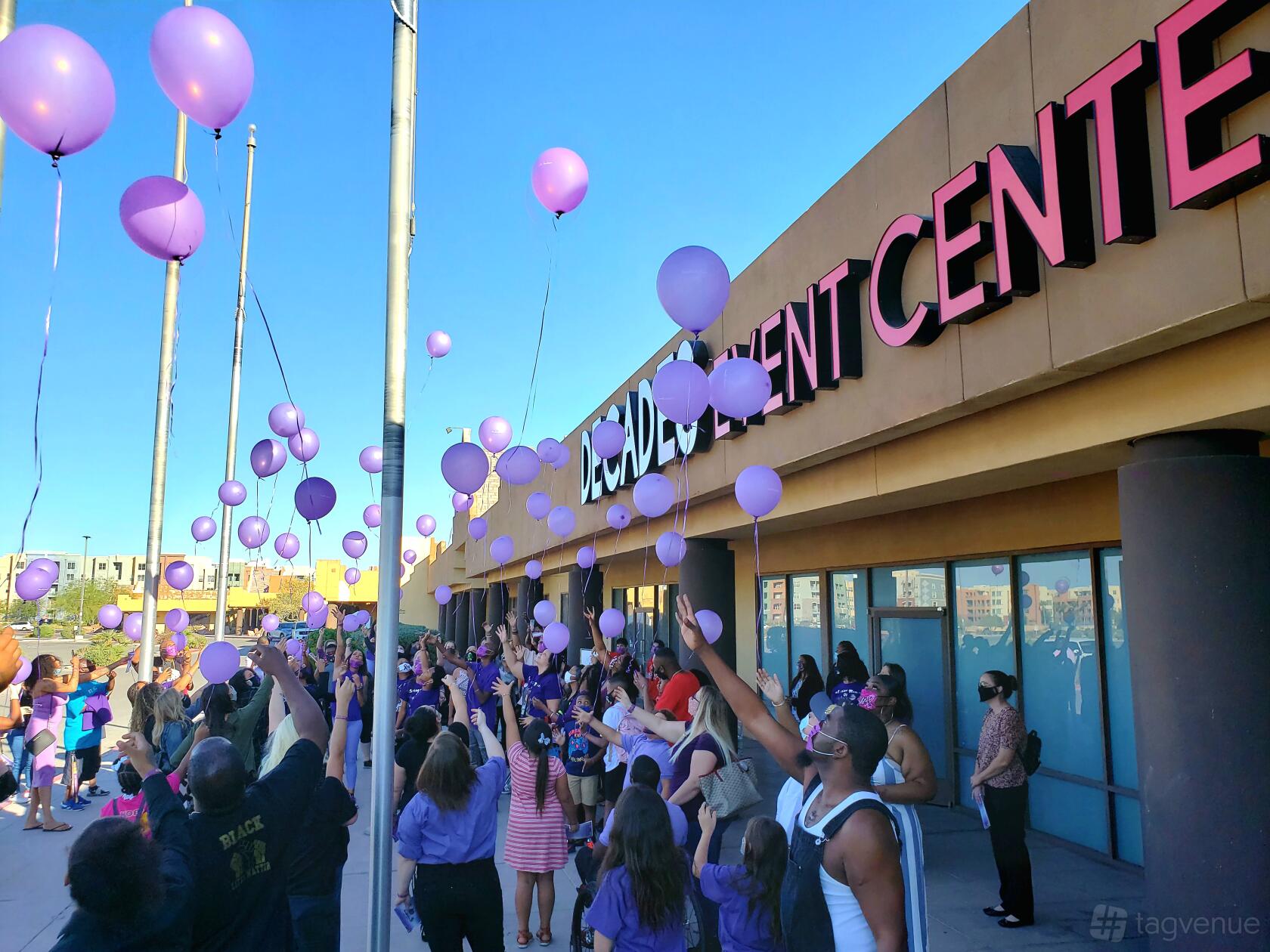 An event hall exterior with a crowd releasing purple balloons in front of Decades Event Center.