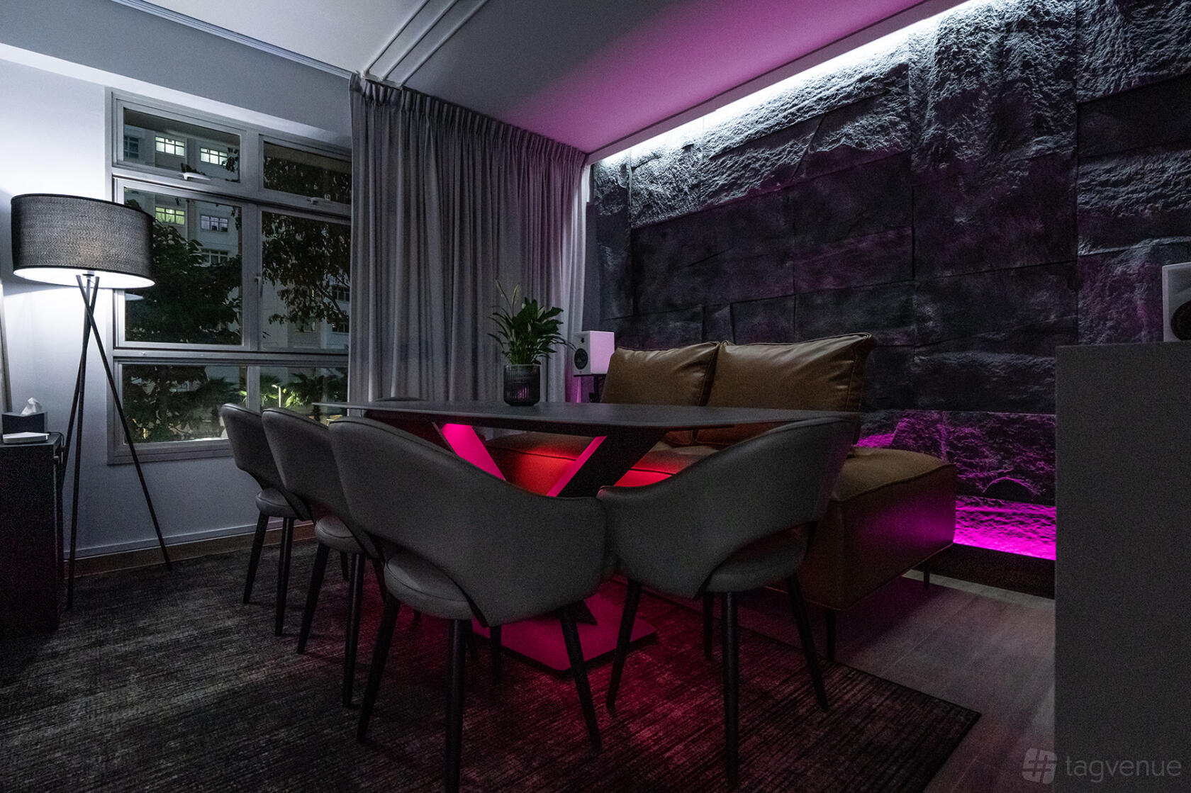 A dining area with a long table, modern chairs, faux stone accent wall, and pink LED lighting at Delon's Kitchen.