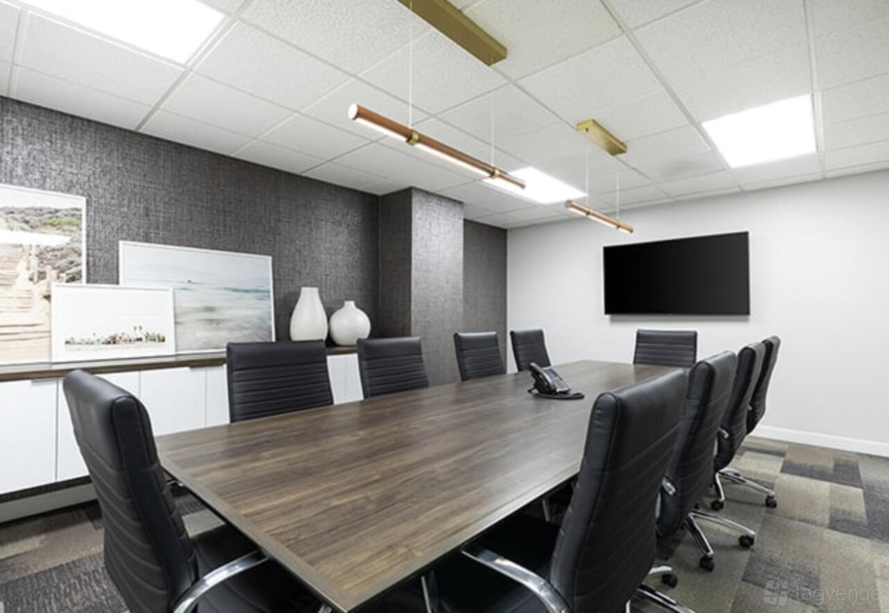 A coworking space with a long wooden conference table, black leather chairs, and wall-mounted TV at Premier Workspaces - Mission Valley.