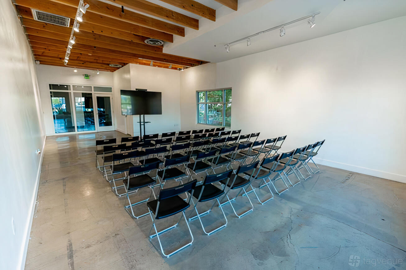 An event venue with rows of black folding chairs, exposed wooden ceiling beams, and a large monitor at Suite 150.