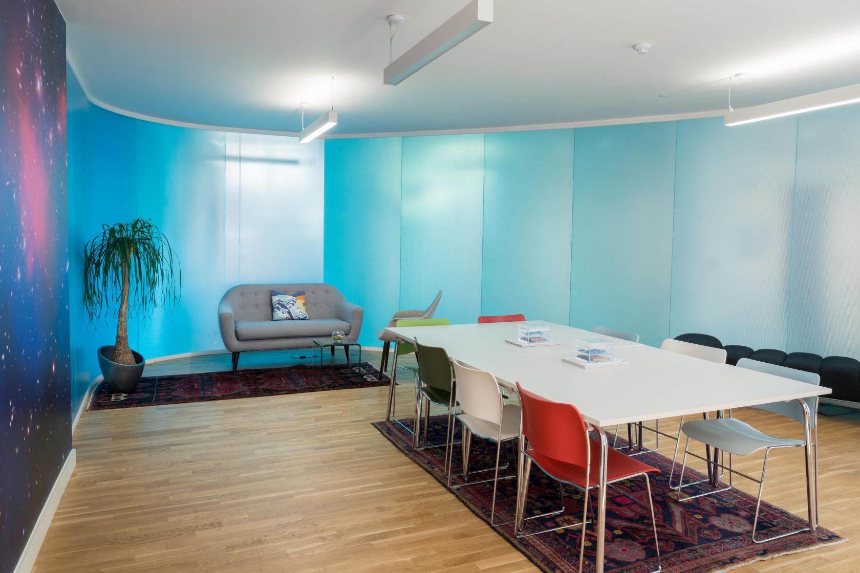 A meeting room with white tables, colorful chairs, a gray sofa, and blue gradient walls at Wallacespace Spitalfields.