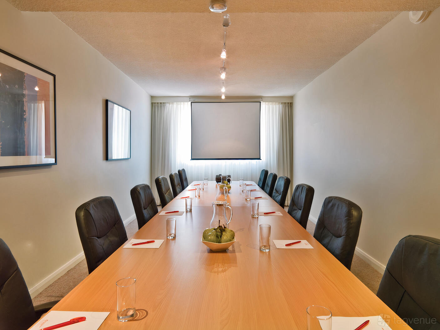 A hotel boardroom with a long wooden table, black leather chairs, and a projector screen at Mercure Perth on Hay.