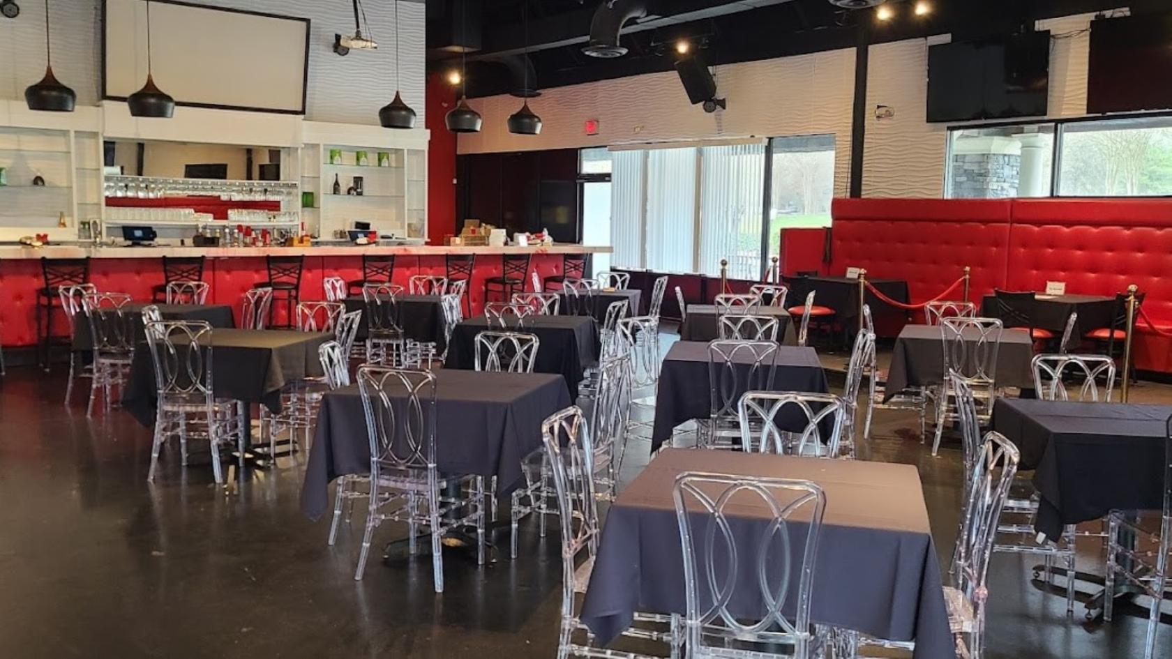 A restaurant with clear acrylic chairs, black tablecloths, and red banquette seating at 592 Lounge.