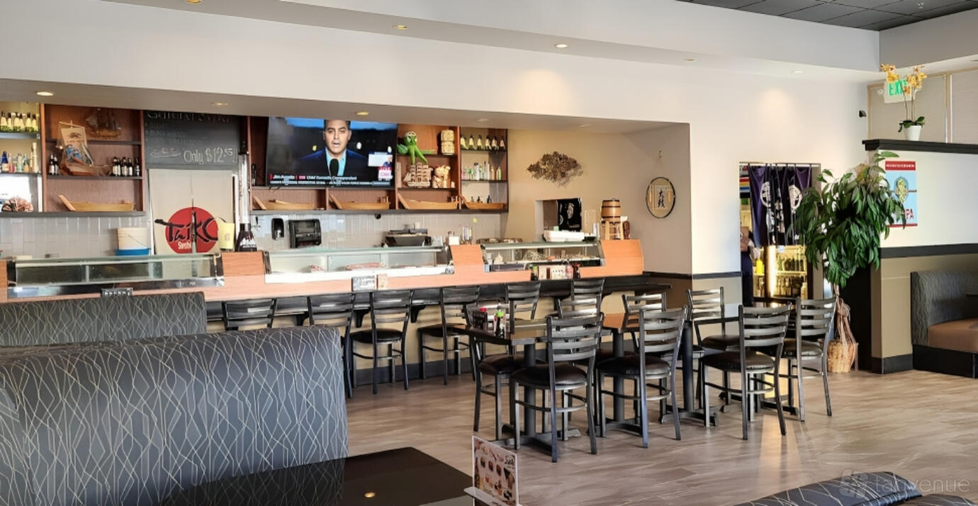 A restaurant with wooden tables, black chairs, a sushi bar, and a television above the counter at Taiko Sushi.