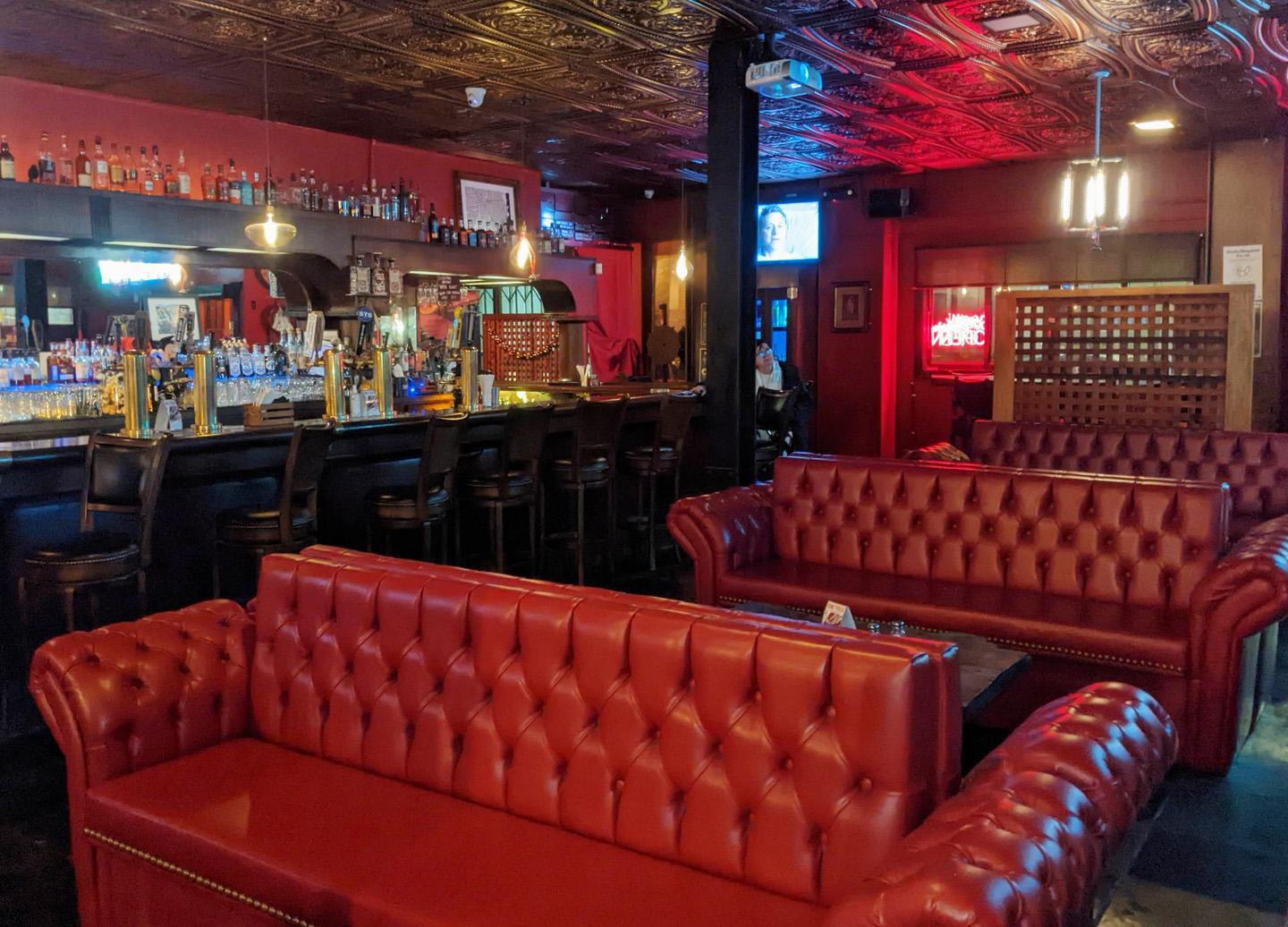 A bar with tufted red leather sofas, dark wood finishes, and a long counter lined with barstools at Shovels Bar & Grill.