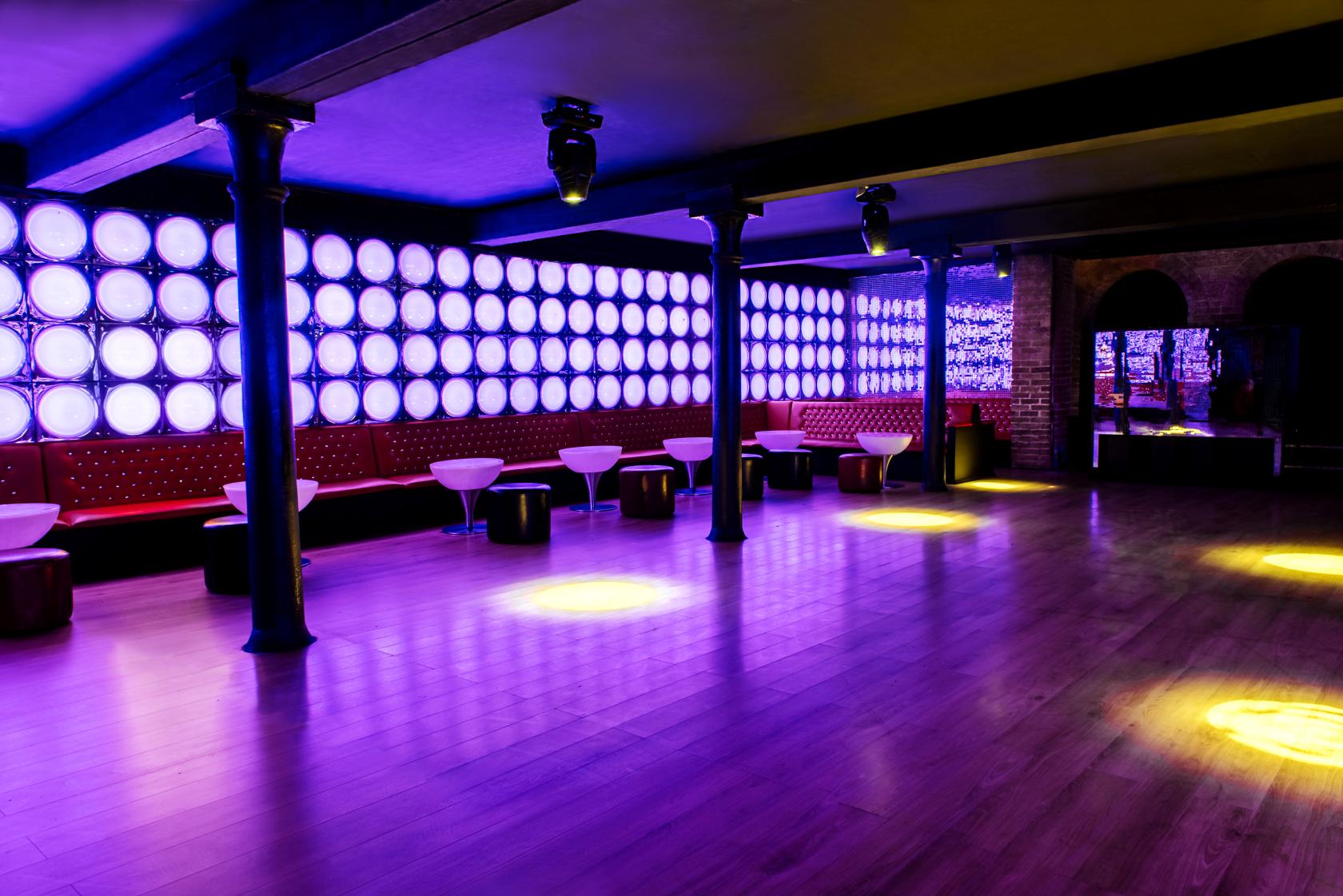 An event space in a nightclub with purple LED wall panels, wood flooring, and red banquette seating at La Pollera Colora.