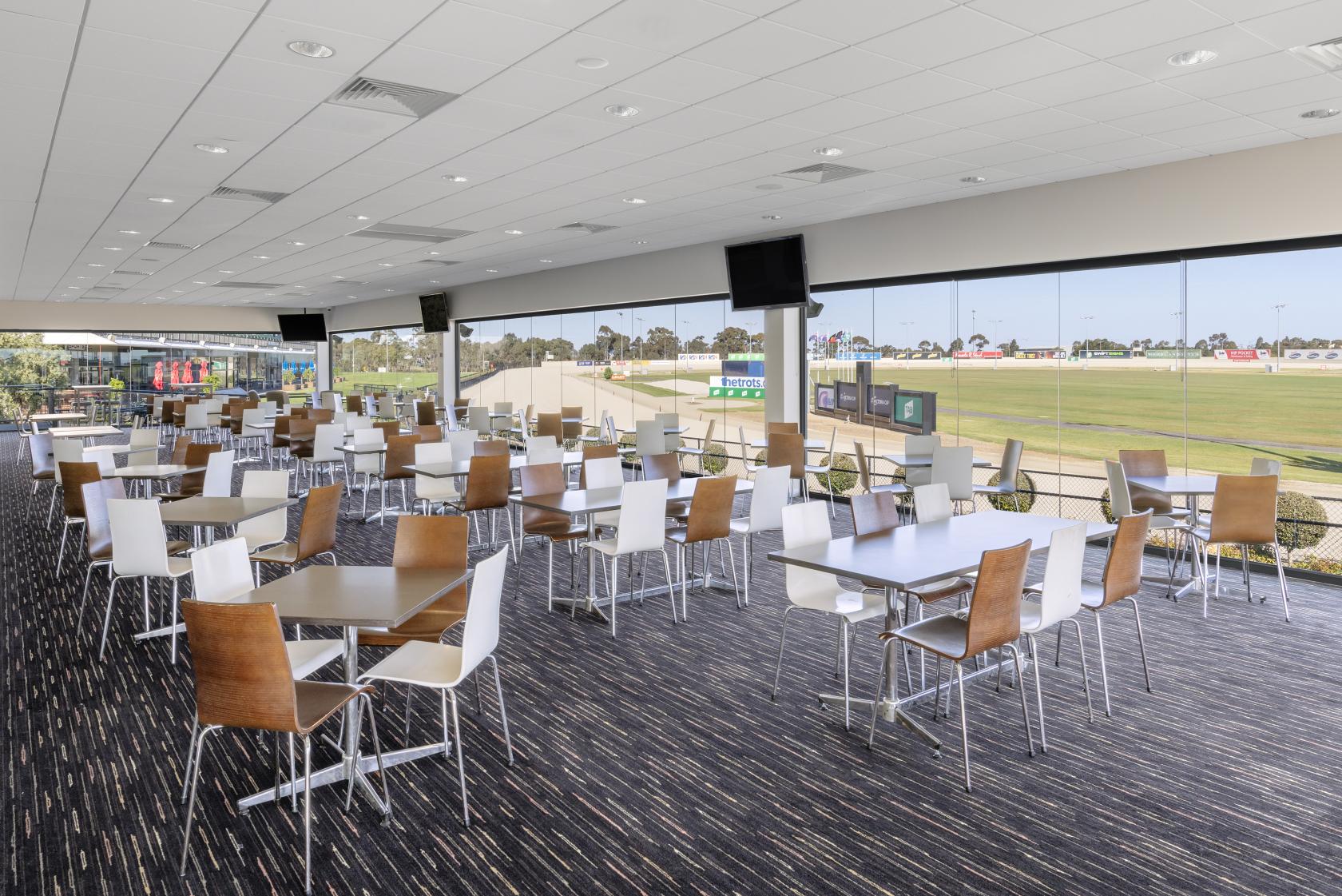 An event venue with floor-to-ceiling windows, rows of white and wood chairs, and field views at Melton Entertainment Park.