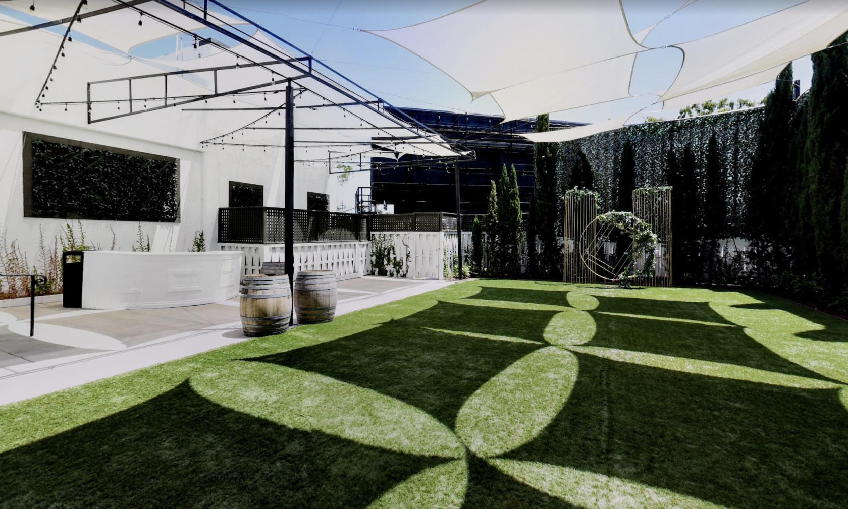 An outdoor event venue with artificial grass, string lights, and geometric shade sails at VASA Rose Garden.