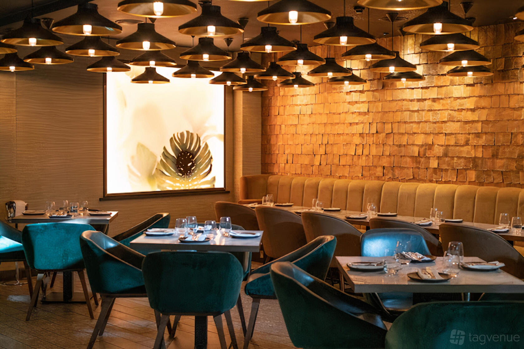 A restaurant with velvet chairs, wooden tables, and warm overhead lighting at Farzi London.