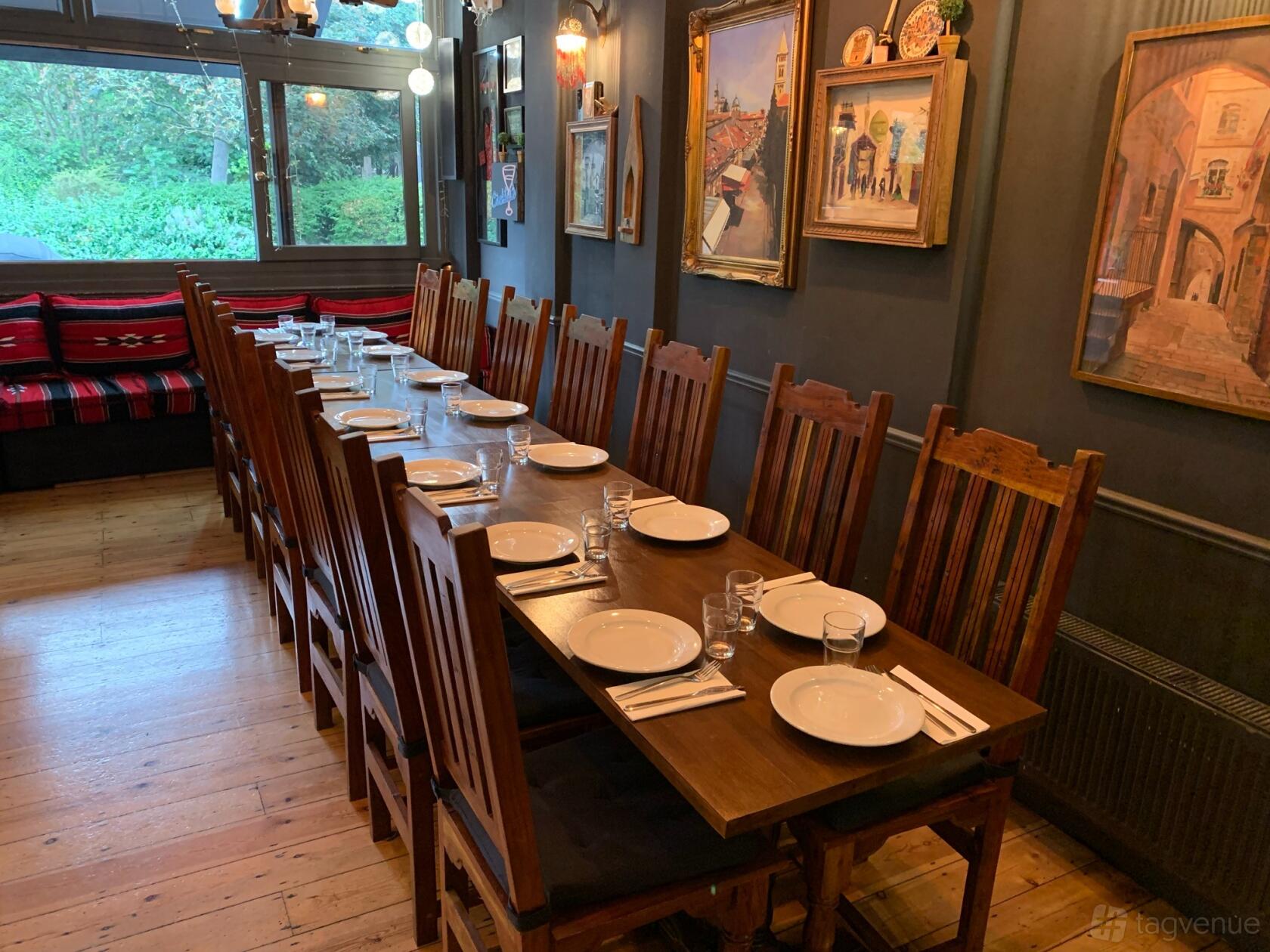 A restaurant with a long wooden dining table, high-back chairs, wood floors, and framed artwork at Mora Meza Bar & Restaurant.