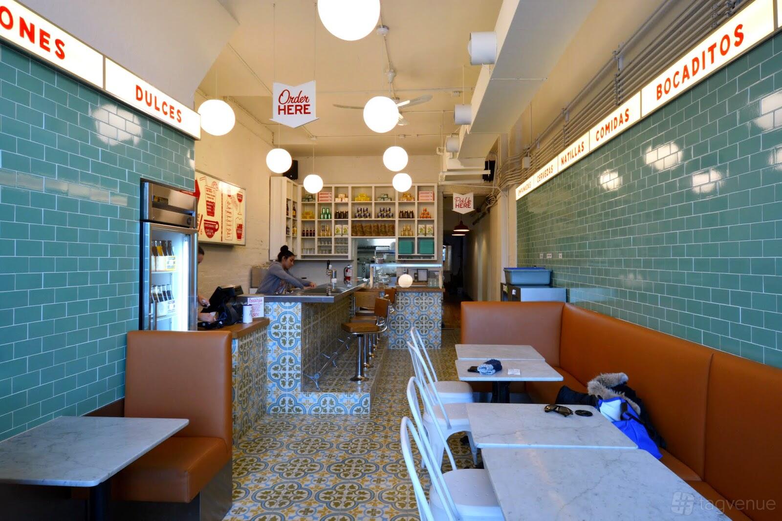 A restaurant with teal tiled walls, patterned floor, marble tables, and round pendant lights at La Cubana - OSSINGTON VILLAGE.