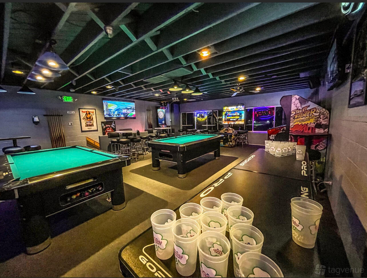 A bar with pool tables, arcade games, and beer pong tables under exposed beams at The Blue Moon Lounge.