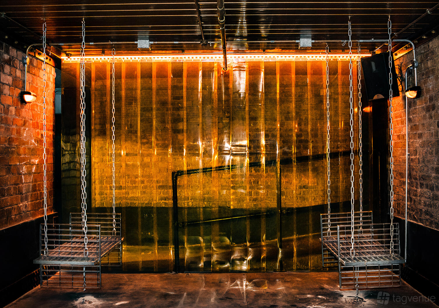A bar area with metal chain swing seats, exposed brick walls, and orange strip lighting at fabric industrial arts events venue.