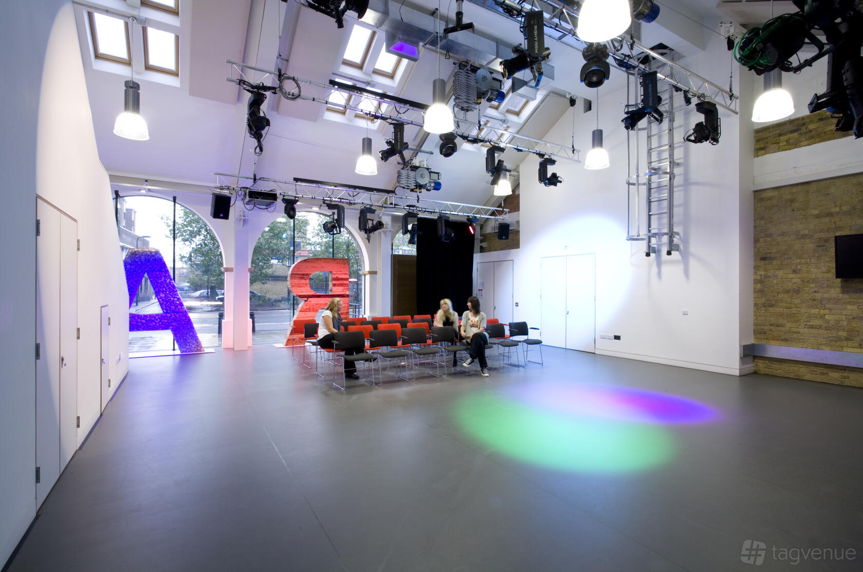 A rehearsal room with high ceilings, stage lighting, skylights, and tiered seating at Graeae Theatre Company.