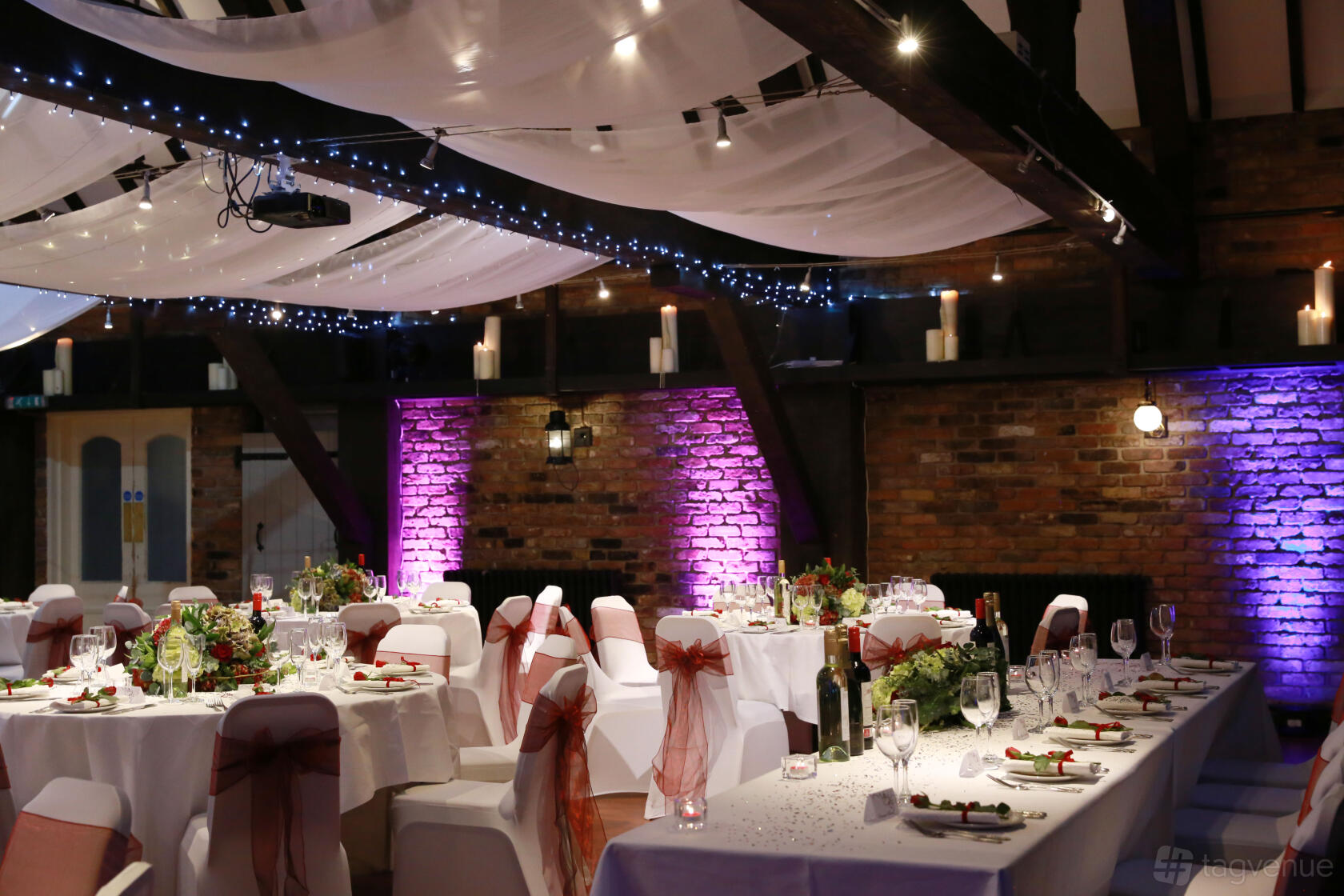 A function room with draped fabric ceiling, exposed brick walls, round tables with white linens at The Dickens Inn