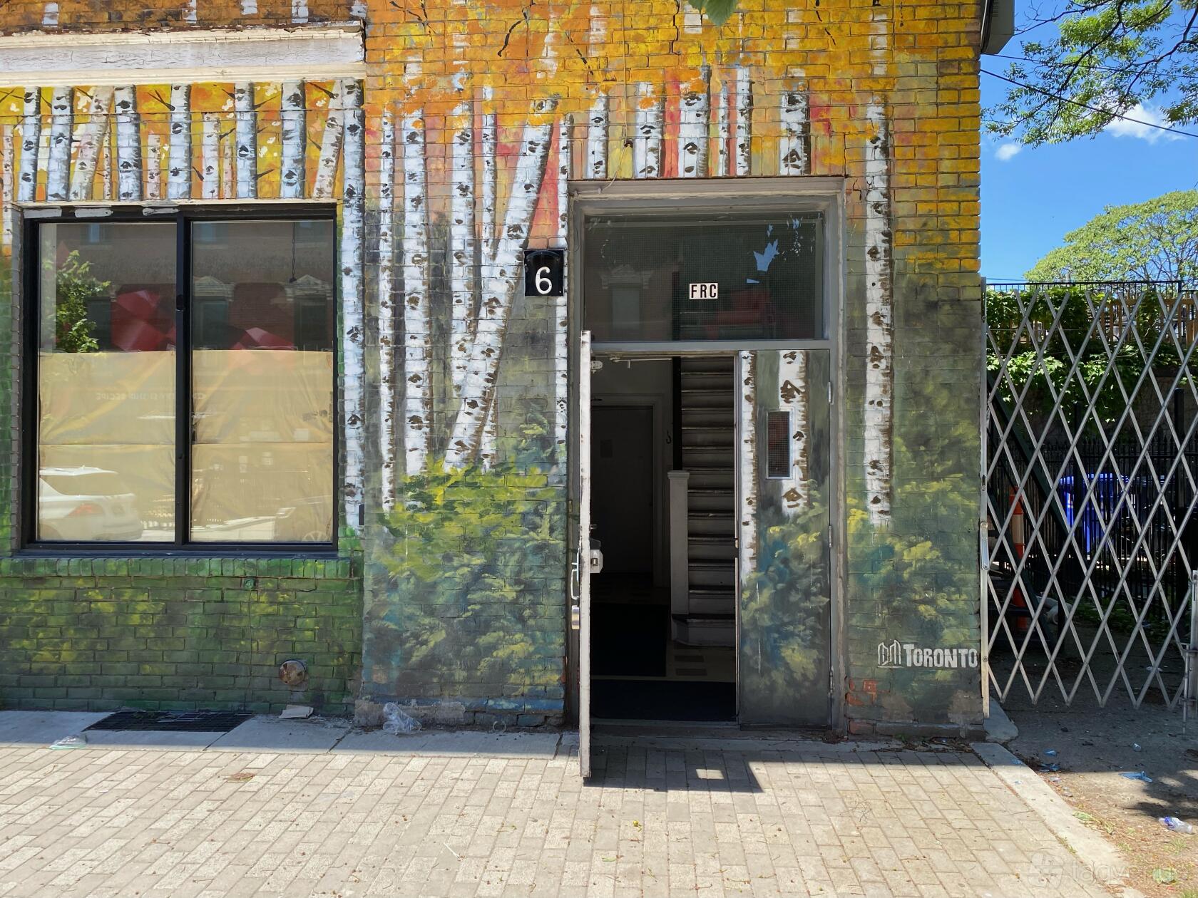 A recording studio with a mural of birch trees on a yellow brick exterior and a numbered entrance at Secret Weapon Sound.