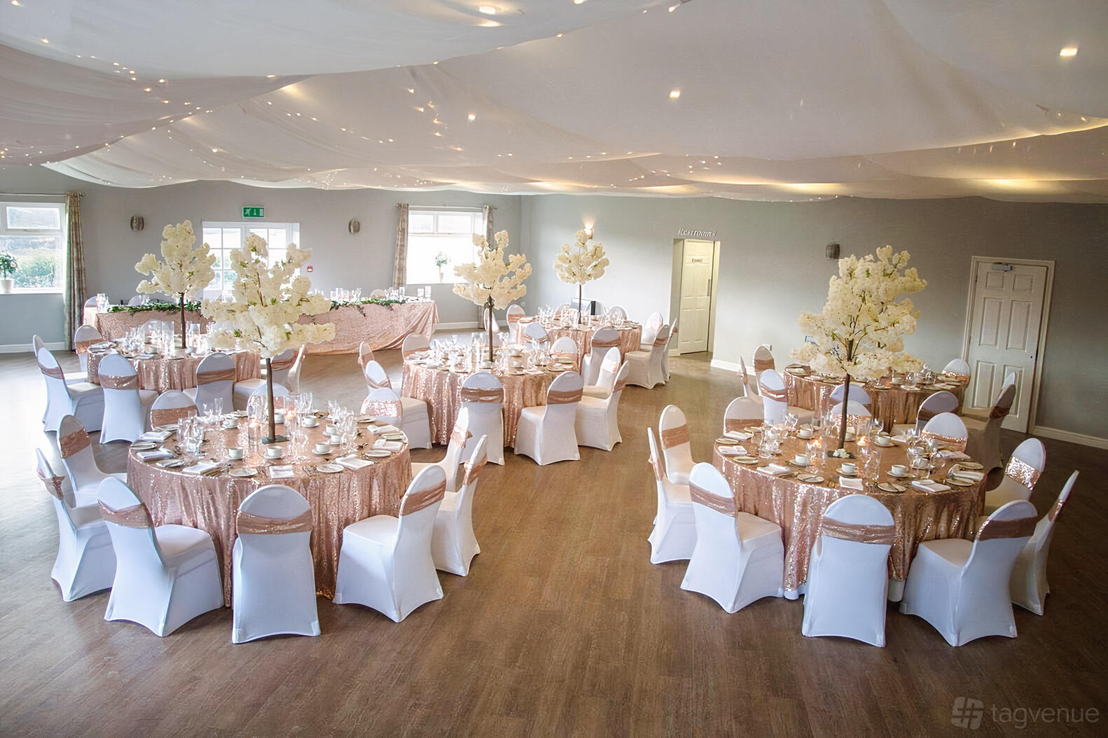 A function room with round tables covered in pink sequin tablecloths and white floral centerpieces at The Dunes Hotel.