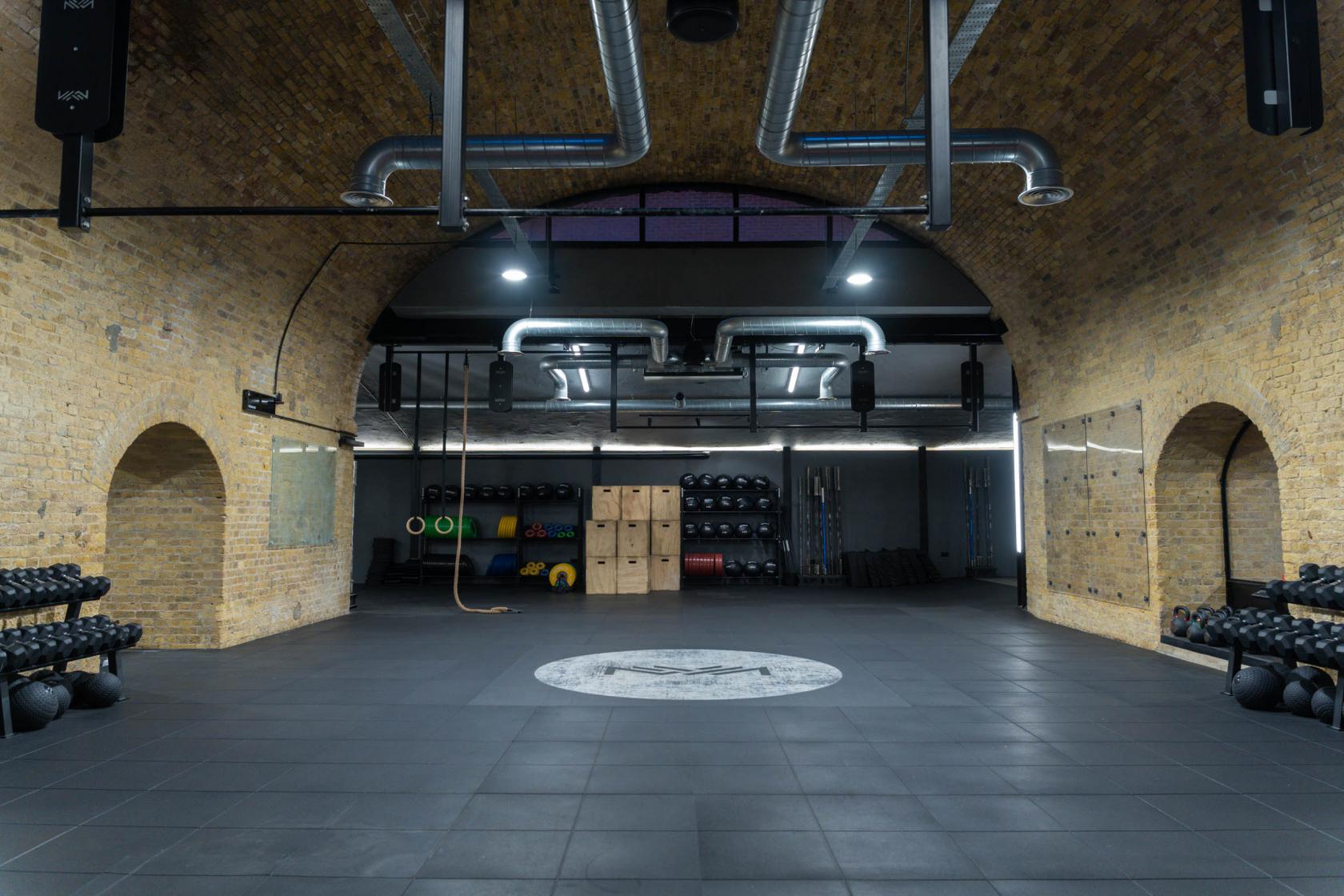 A fitness studio with exposed brick arches, wall mirrors, and gym equipment storage at CrossFit Putney.