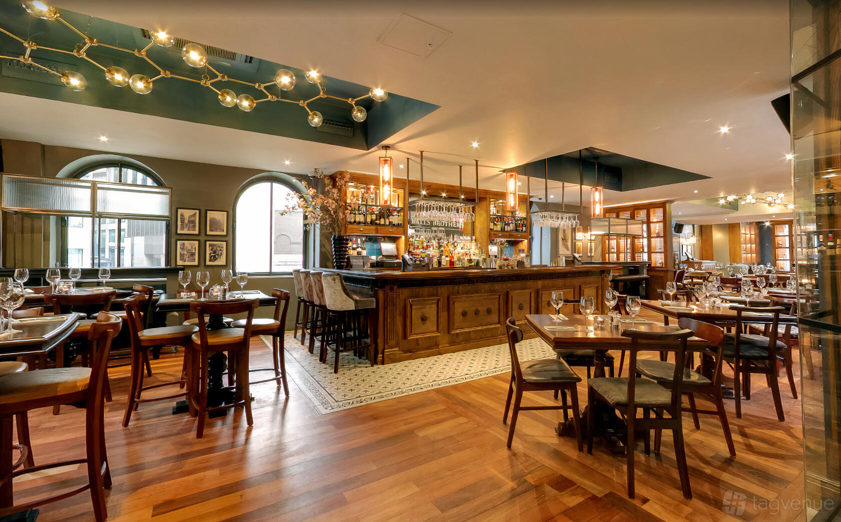 A bar with a central wooden counter, arched windows, pendant lighting, and dining tables at Andrea Adam's Court.
