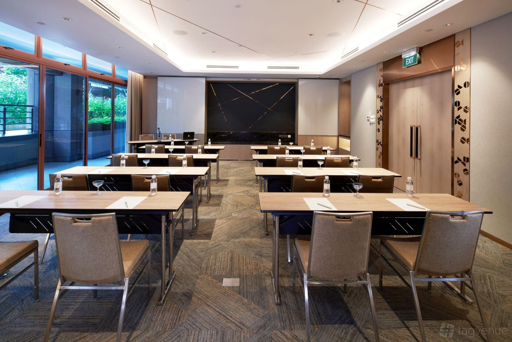A hotel meeting room with classroom seating, floor-to-ceiling windows, and bottled water at Orchard Grand Court.