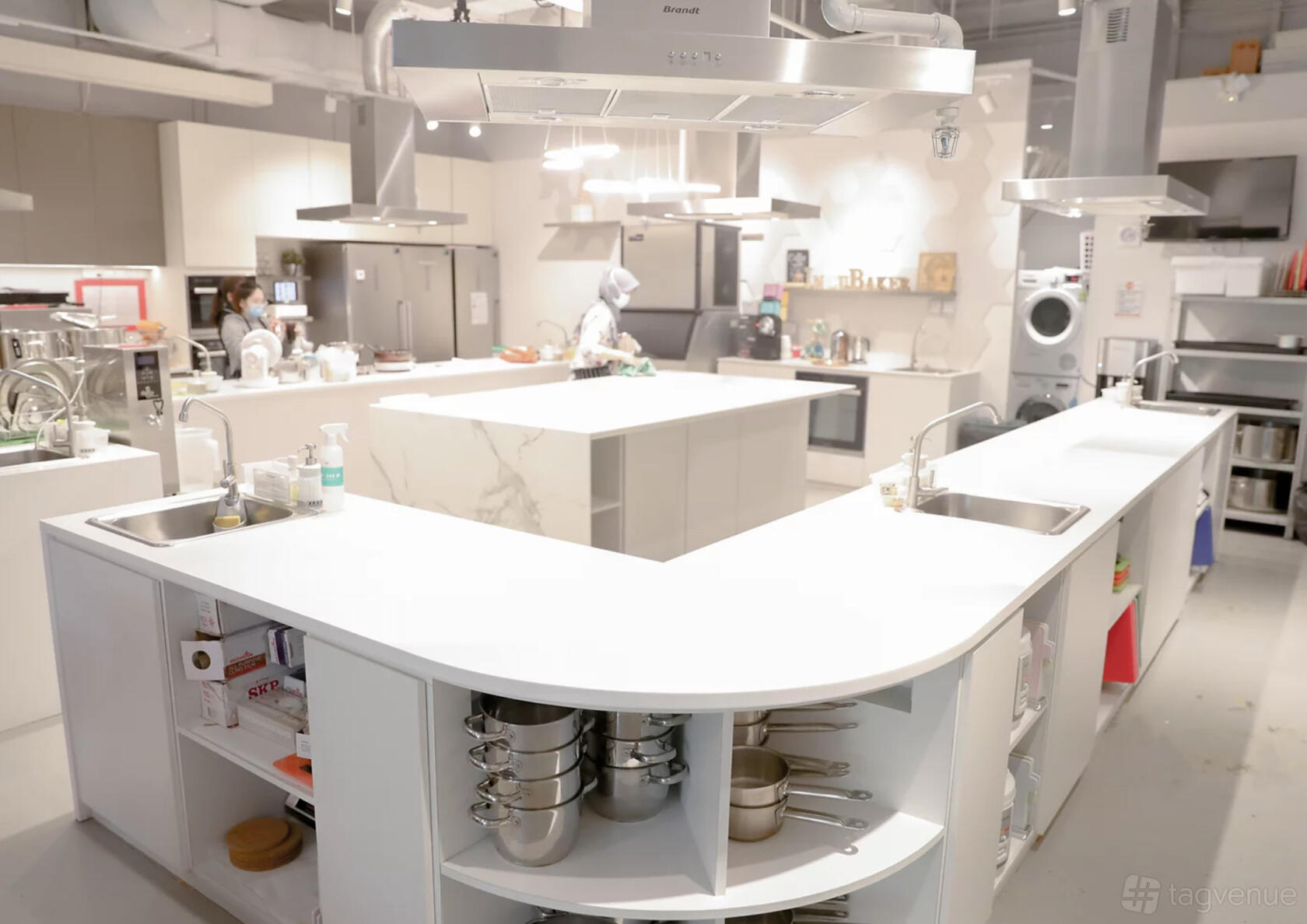 A kitchen with double sinks, open shelves of cookware, and a central island workstation at IncuBaker.
