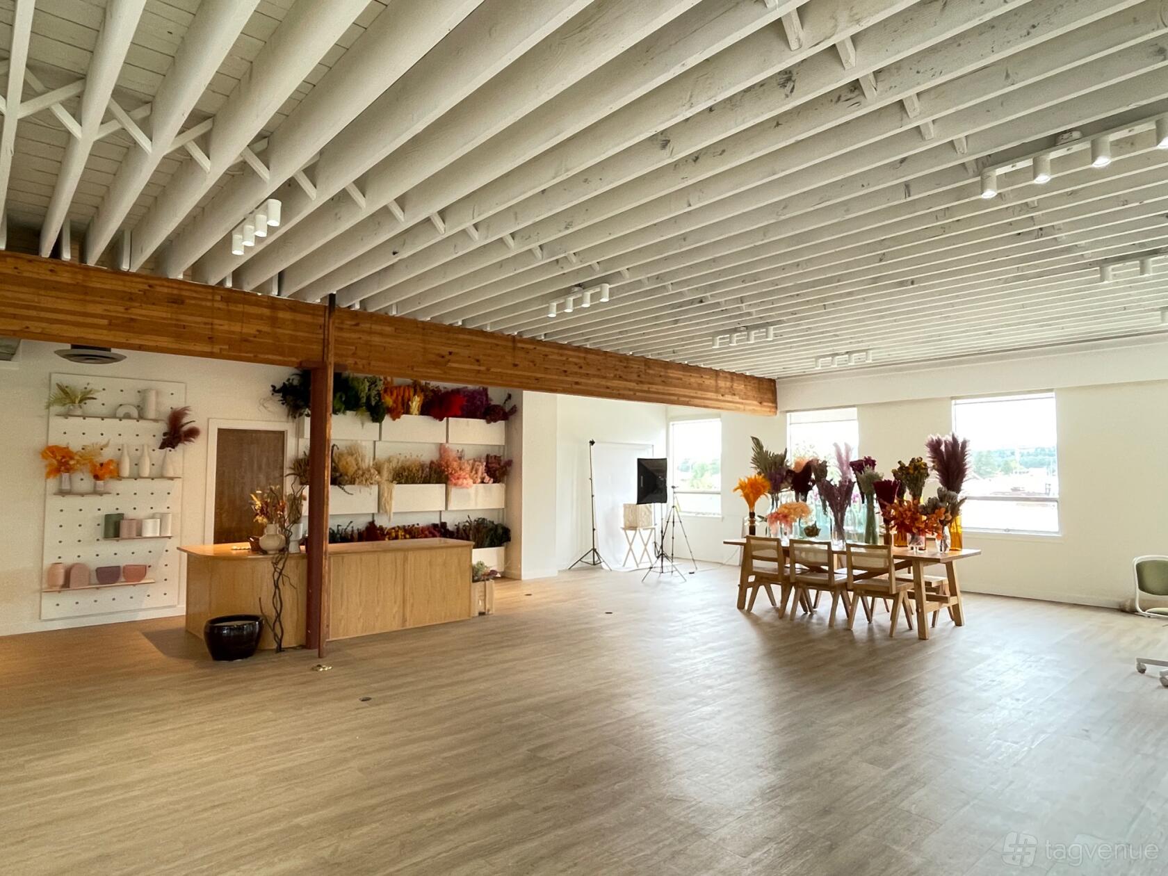 A meeting room with exposed ceiling beams, large windows, and a table decorated with dried flowers at DB Studios.