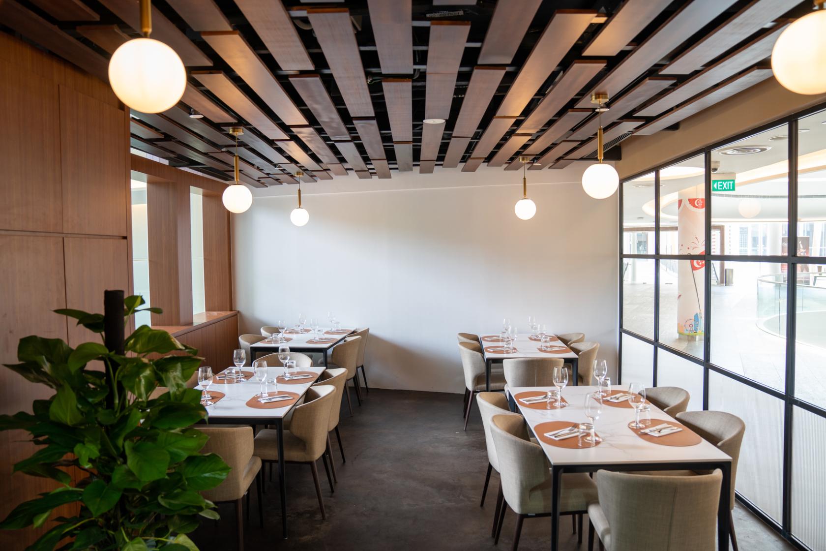 A restaurant with round pendant lights, wooden accents, and tables set with white linens at Casa Pietrasanta.