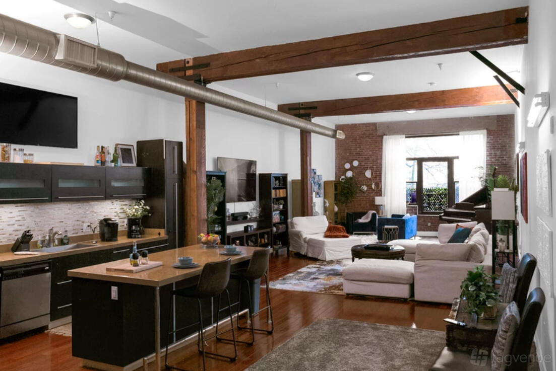 A loft with exposed brick walls, wooden beams, an open kitchen, and lounge seating at LTE Studio Loft.