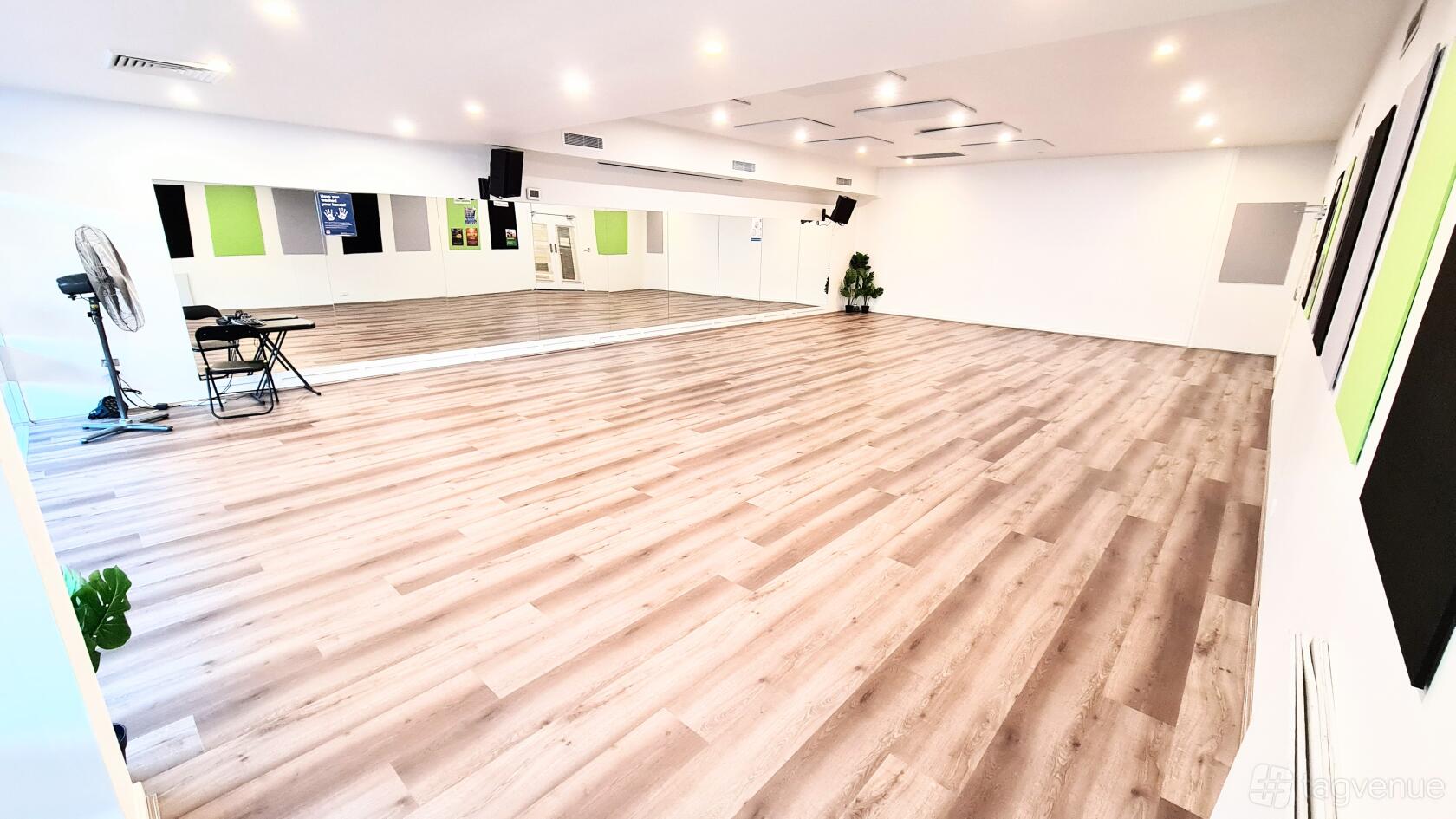 A dance studio with wood floors, mirrored wall, ceiling lights, and a few chairs at Tropical Soul Dance Studio.