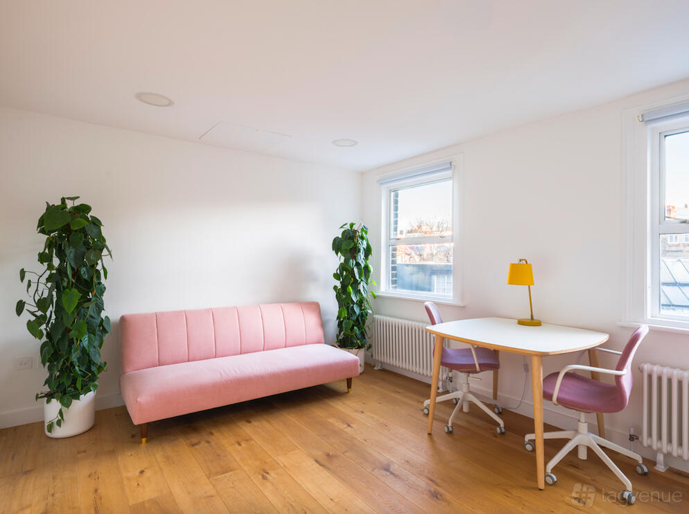 A meeting room with a pink sofa, two potted plants, and a small white table with pink chairs at Mimosa House.