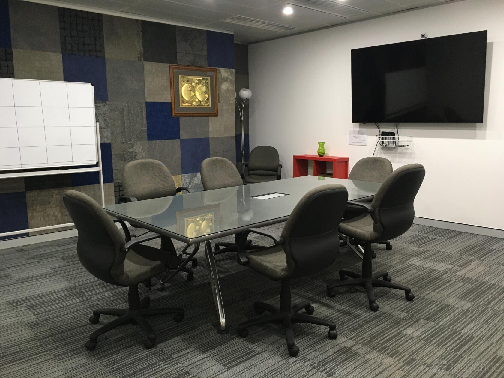 A meeting room with a glass table, rolling chairs, whiteboard, and wall-mounted monitor at A23.