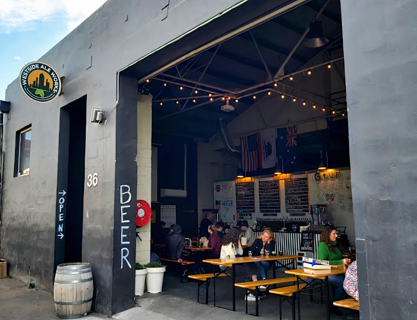 A pub with communal wooden tables, string lights, and wall-mounted beer taps at Westside Ale Works.