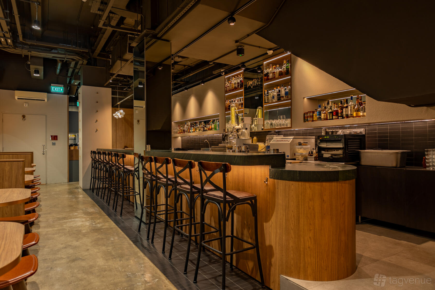 A cocktail bar with a long wood counter, high black stools, and shelves of liquor bottles at The Elephant Room Singapore.