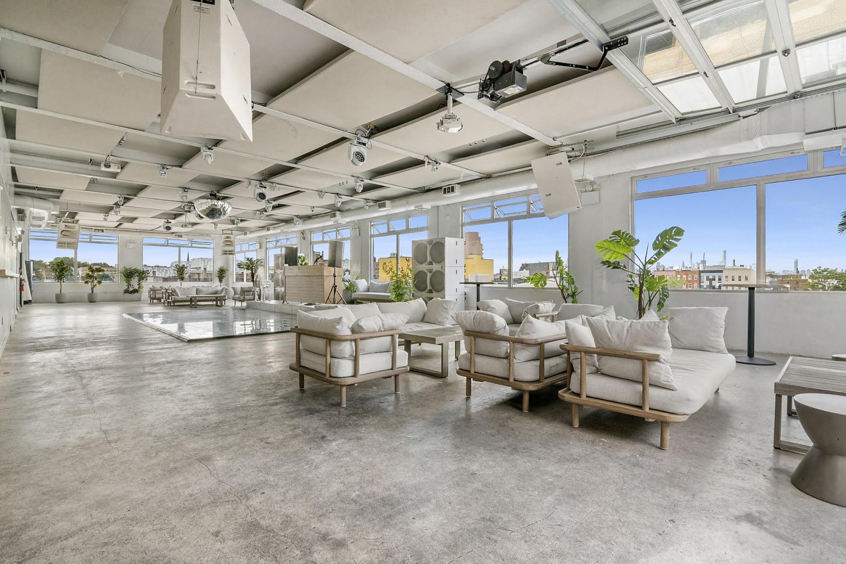 An event space in a penthouse with floor-to-ceiling windows, white lounge seating, and potted plants at Bogart House.