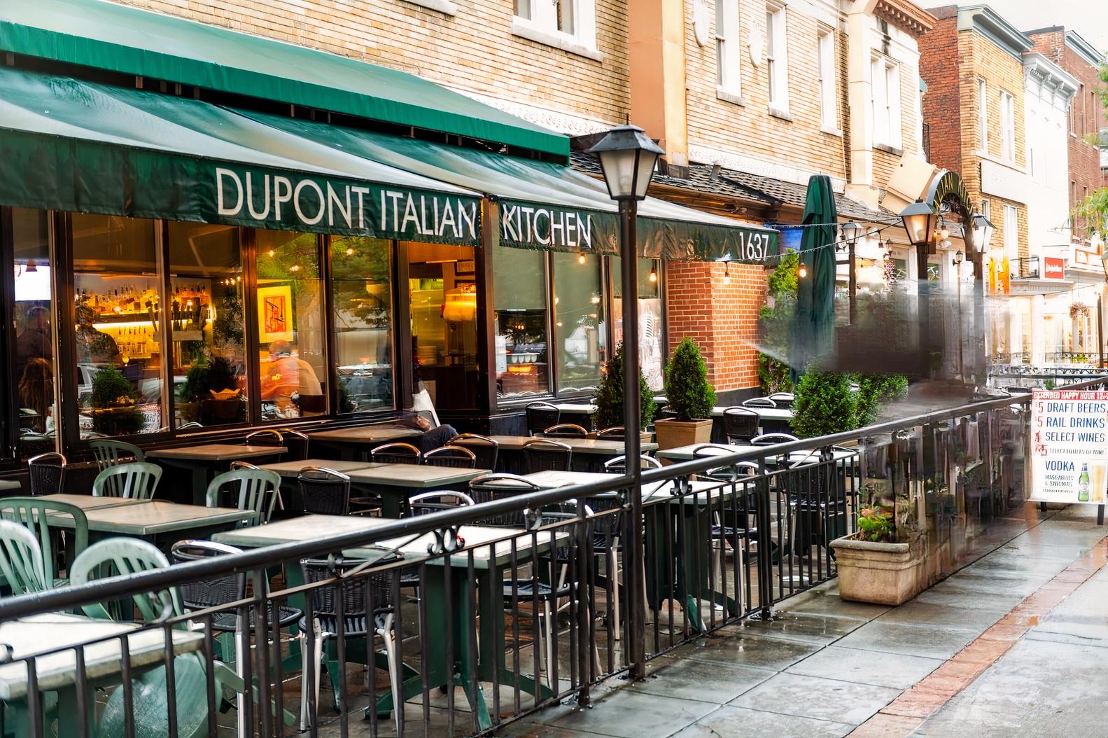 An outdoor restaurant patio with green chairs, tables, and an awning at Dupont Italian Kitchen.