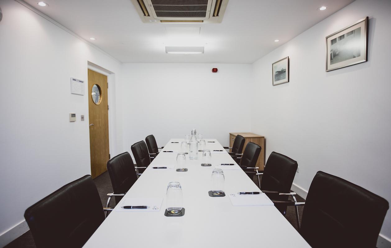 A meeting room with a long white table, black chairs, and minimalist decor at Orega - The Beehive - Gatwick.