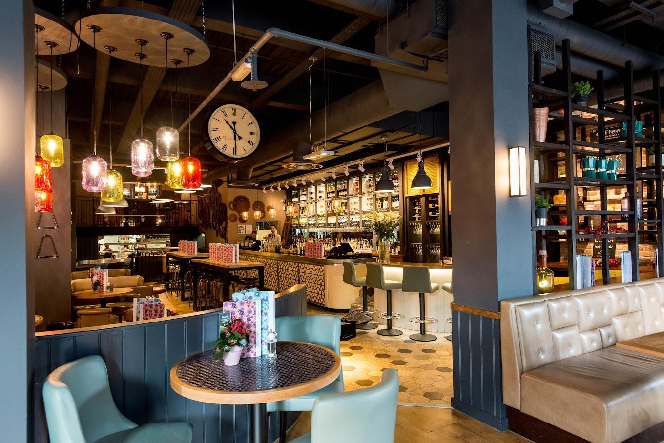 A lively bar with pendant lighting, cushioned booths, and a long counter with barstools at All Bar One Manchester.