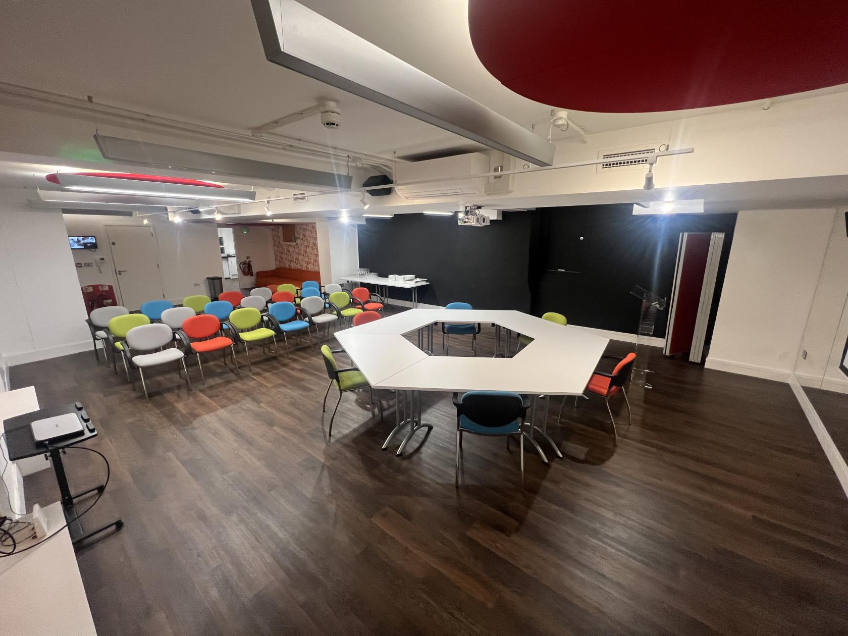 An event venue with hexagonal white tables, colorful chairs, and dark wood floors at Warren Centre.