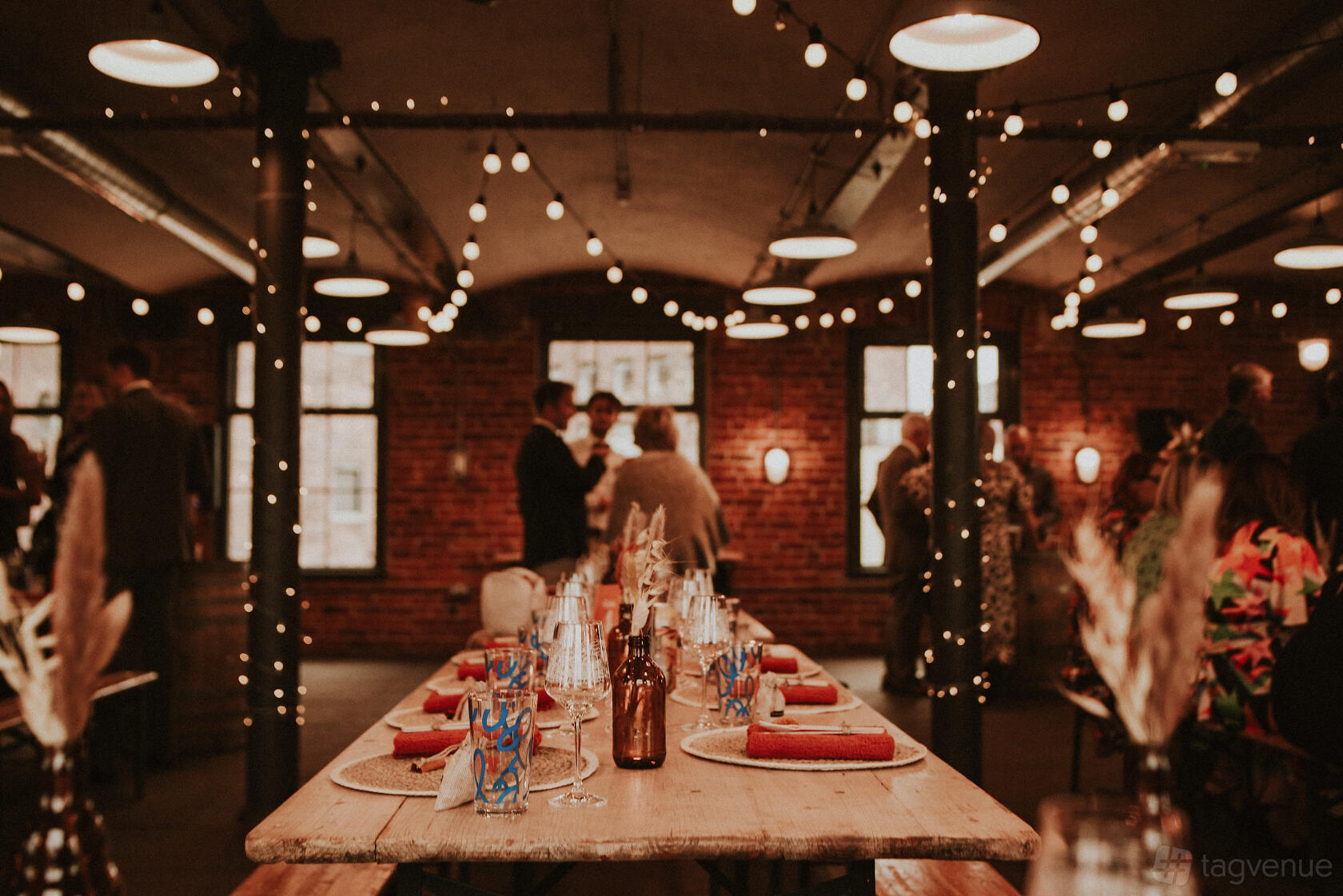 An event venue with exposed brick walls, string lights, and a long banquet table set for dining at The Chapter Hall.