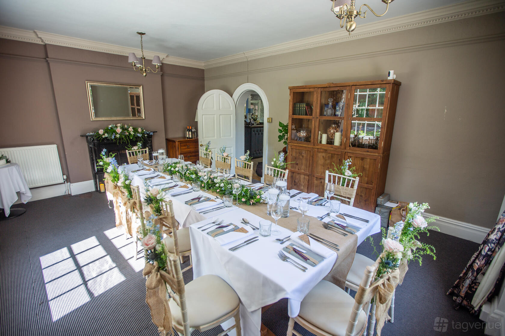 A dining room with U-shaped table arrangement, white linens, floral centerpieces, and natural light at Old Rectory House.